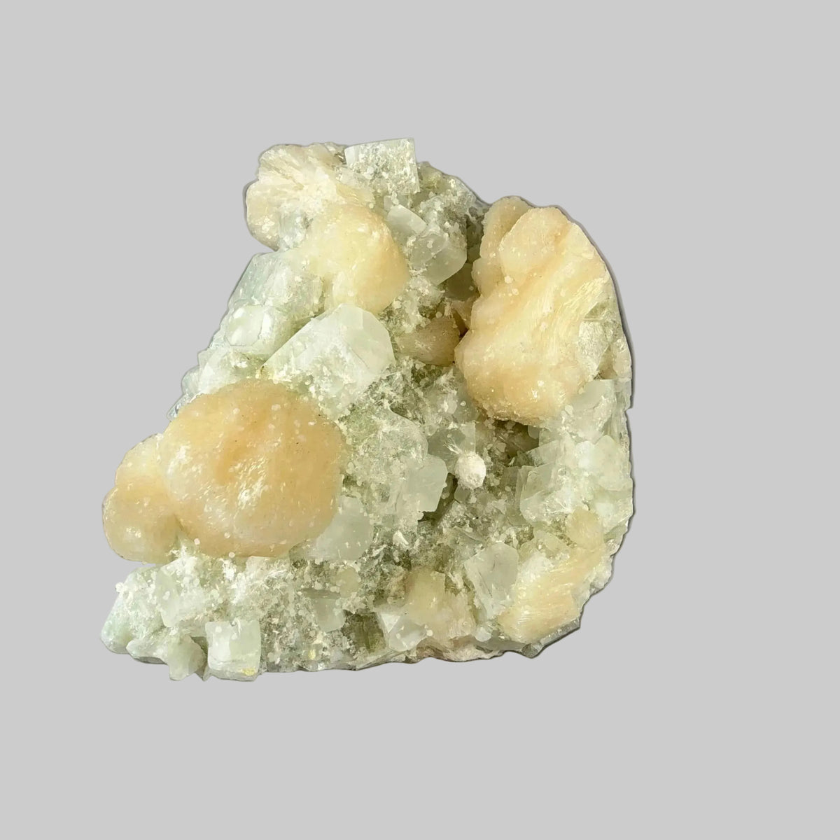Indian zeolite mineral specimen with peach and cream crystal clusters among pale green and translucent crystals, shown against a dark background.