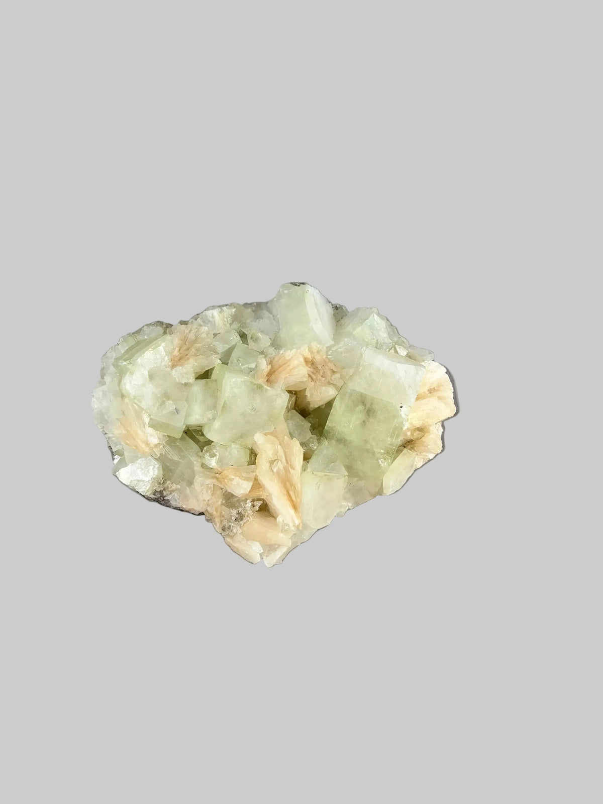 Indian zeolite mineral specimen with prominent pale green translucent crystals and smaller peach and cream formations against a gray background.